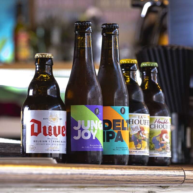 Selection of beers at Jungle Joy's bar: Duvel, Jungle Joy, Delta IPA, La Chouffe Blonde, and La Chouffe IPA on a bar table with a vibrant and blurry background.