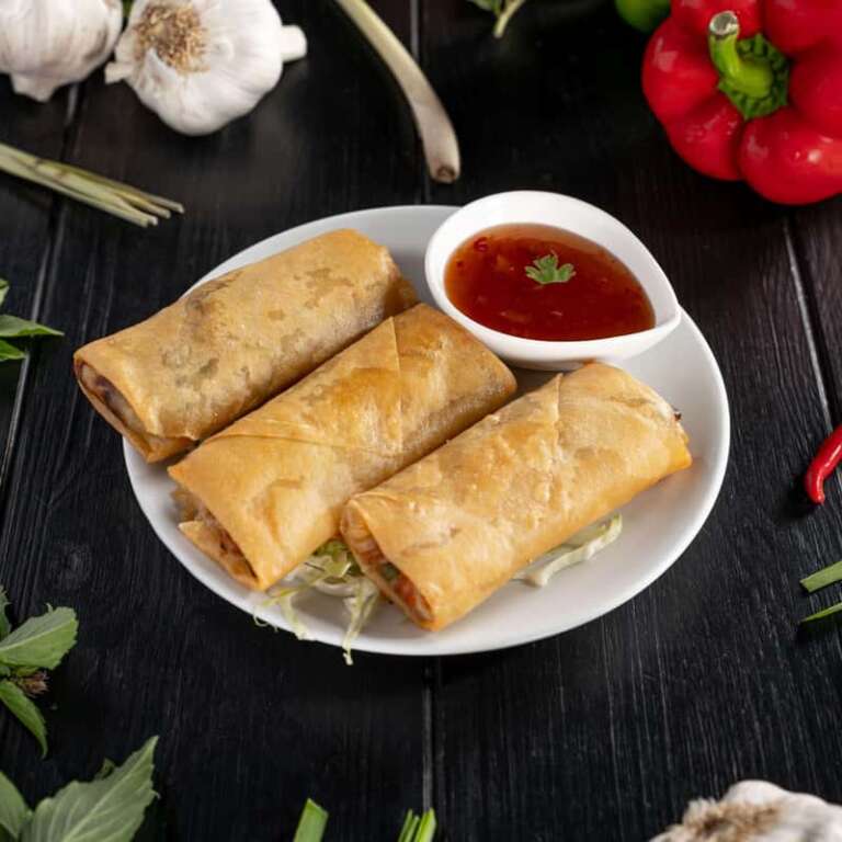 Three pieces of vegetarian spring rolls on a plate with sweet and sour sauce on the side.