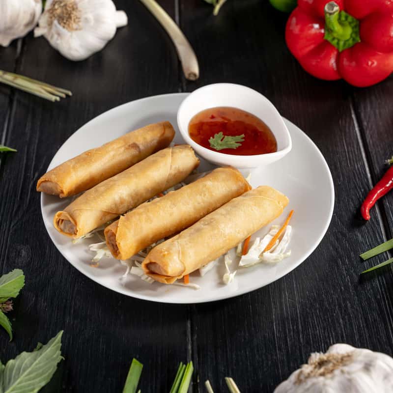 Four pieces of duck spring rolls on a plate with sweet and sour sauce on the side.