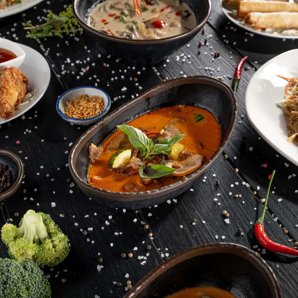 Red curry and assortment of Thai dishes on a black wooden table.