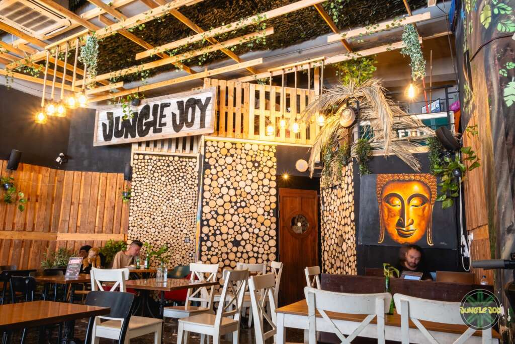 Inviting Interior of Jungle Joy Venue: Wood Panel Roof, Hanging Plants, and Warm Yellow Lighting.