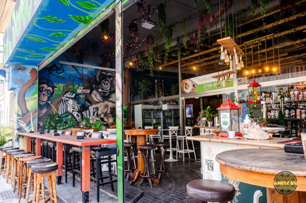 Enchanting Outdoor Setting at Jungle Joy Venue: Hanging Plants, Artistic Animal Murals, Abundant Seating, and a Well-Stocked Bar